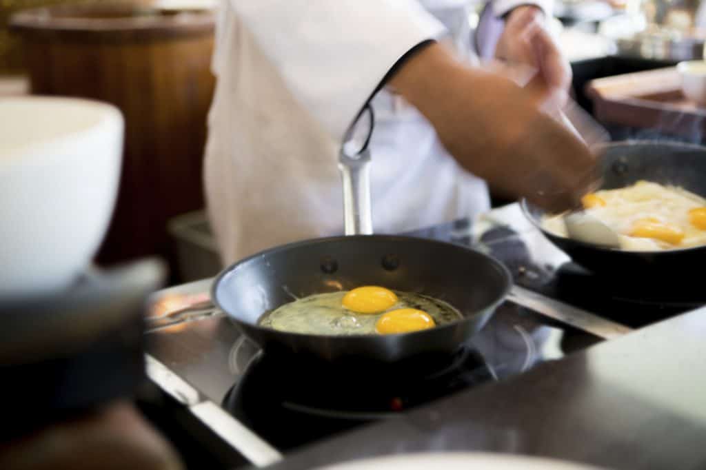 Close up of a chef working on omelets in multiple pans